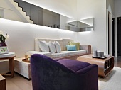 Moderner Wohnraum mit violettem Polstersessel vor Couchtisch im Retrostil und indirekter Beleuchtung hinter Spiegelpanelen an Wand