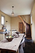 Simple wooden table in open-plan dining room with kitchen area and staircase in background