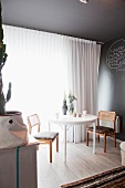 White round table and chairs next to window with airy curtain in grey-painted interior