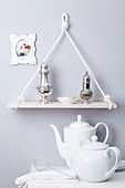 Shelf made of plank and rope hanging above teapot and coffee pot on table