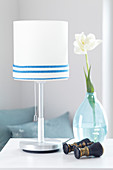 Table lamp decorated with cord, tulip in glass vase and binoculars