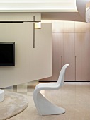 Klassiker Schalenstuhl aus weißem Kunststoff und zeitgenössischer Raumteiler mit aufgehängtem Fernseher