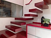 Floating stair treads of reddish wood and sideboard below staircase