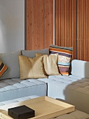 Cushions on light-coloured corner sofa in front of cupboard with door made of wooden slats