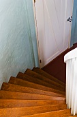 Blick von gewendelter Holztreppe nach unten auf weiße Brettertür und pastellblaue Wand