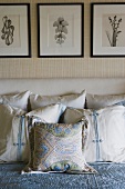 Gemusterte Kissen und Decken auf Doppelbett mit gepolstertem Kopfteil unter gerahmten Pflanzenfotos