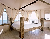 Hand-made bed crafted from weathered beams on castors in bedroom with panoramic view