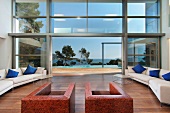 Sesseln aus Leder und helle Sofagarnitur im minimalistischen Wohnraum mit offener Glasfassade