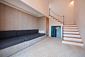Eingebaute Bank mit schwarzen Sitzpolstern vor Holzwand und offene Treppe im minimalistischen Vorraum