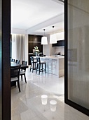 Mattes Schwarz und spiegelndes Weiß in offenem Wohnraum mit Barhockern an der Küchentheke