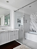 Weisses Designerbad mit Materialmix aus geflammten Marmorflächen, Mosaikfliesen und dunklem Holzboden