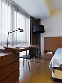 Work area with a floor lamp in front of a window in a modern bedroom