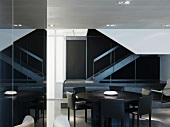 Runder Tisch aus dunklem Holz mit grauen Stühlen vor Treppenaufgang im minimalistischen Raum