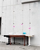 Antique wooden table with mismatched table elements added on against concrete wall