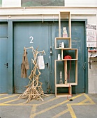 Artistic coat rack made of coathangers next to modern wooden shelving in front of grey metal doors
