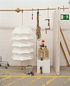 Stacked white umbrellas and clamps hanging from wooden rod above tower of cubes