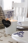 Lit tealight in metal bucket with heart-shaped, blackboard place name on set table