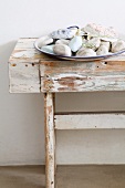 Plate of pebbles and shells on old wooden bench with weathered white paint