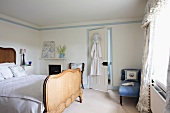Antikes Doppelbett mit hohem Kopf- und Fussteil aus Naturholz und hellblau gemusterte Recamiere in lichtem Schlafzimmer mit Schabrackenvorhang im Nostalgieflair.