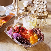 Silber-Korb mit künstlichen Früchten vor Tischleuchte mit Kristallschmuck