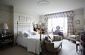 Antique country-house bedroom with metal four-poster bed, upholstered furniture and floral curtains with pelmet