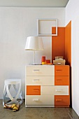 Dark orange accents on white chest of drawers and wall in corner of room