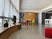 Moderner offener Wohnraum mit geschwungener Fensterbank aus Holz und Essplatz mit farbigen Stühlen