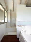 Doppelbett vor einem Raumteiler-Schrank zum Bad Ensuite; weiss lasierte Deckenbalken und seitlich durchgehendes Fensterband