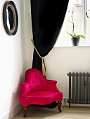 Pink armchair in from of a black, velvet curtain in the corner of a room
