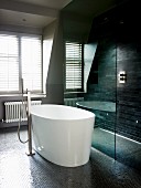 White, free-standing designer bathtub with standpipe tap fittings on dark mosaic floor next to shower area