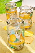 Lit hurricane candles in preserving jars with fruit motifs on pale yellow tablecloth