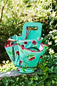 Gardening utensils in turquoise plastic bag with cherry motif on stone wall in garden