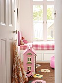 View through open door of dolls' house on floor in front of traditional child's bed below window