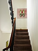 View up staircase with brown carpet and wrought iron balustrade to picture with shoe motif on wall of traditional staircase