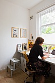 Woman at desk in corner of room below window