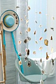 Seashells strung on cords hanging from ceiling in front of wicker chair