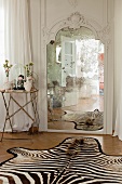 Side table next to antique mirror and zebra-skin rug on parquet floor in bedroom