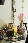Rose in ceramic vase and vintage jewellery on side table