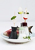Party skewers stuck in lids of salt cellars and wooden fish on plate