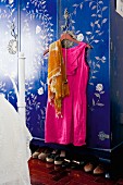 Hot pink dress and scarf on coat hanger hanging on door handle of blue wardrobe with pale floral pattern