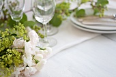 A table laid for a meal and decorated with white roses, baby's breath and ranunculus flowers