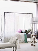 Romantically decorated double bed with voile draped over modern canopy frame; antique-style bedroom bench in foreground