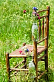 Flaschen mit Wiesenblumen hängen am Holzstuhl