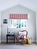 Cozy bamboo chair with adjoining tray table under window with striped roller blind