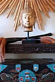 Buddha's head on carved console table below sunburst gilt frame on wall