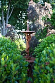 Antique garden sculpture between bushes