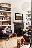 White-painted bookshelves in sitting room with traditional fireplace, old school trunk and grey armchair