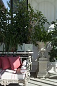 White, wrought iron bench in front of luxuriant potted plants in front of window
