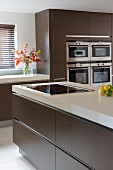 Kitchen island and fitted appliances in designer kitchen with brown cupboard doors