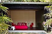 Blick vom Garten in ein modernes Schlafzimmer mit Designerstühlen und Doppelbett in Knallfarben
